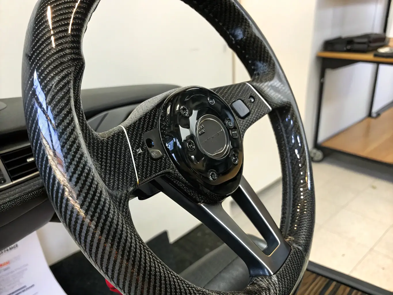 A close-up shot of a Momo Leather Steering Wheel installed in a high-performance vehicle, showcasing its ergonomic design and premium leather finish. The background is blurred to emphasize the steering wheel's sleek aesthetics and sporty appeal.